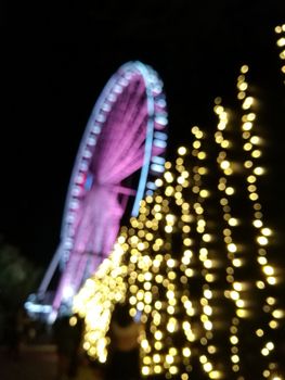 Defocused scene of giant pink flyer ferris wheel at night with yellow light fence