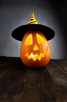 Carved jack-o-lantern halloween pumpkin in witches hat on wooden background