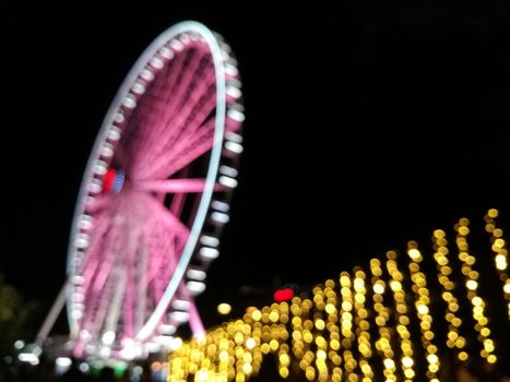Defocused scene of giant pink flyer ferris wheel at night with yellow light fence