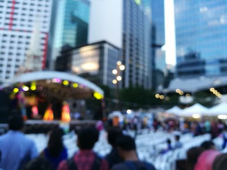 Defocused scene of crowd of people attending public concert celebrating New Year festival in city in Evening