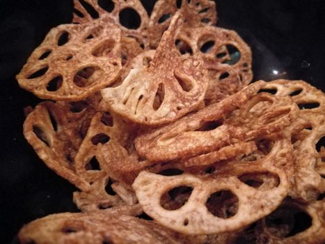 Golden fried crispy lotus root chips in black bowl