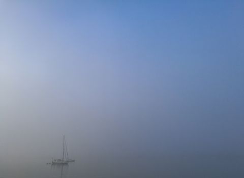 Cold misty ocean with small white yacht floating on the sea in morning