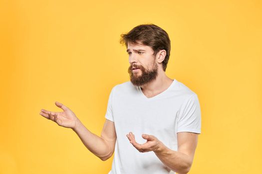 Bearded man in a white T-shirt gestures with his hands emotions studio yellow background. High quality photo