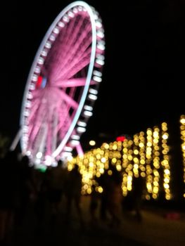 Defocused scene of giant pink flyer ferris wheel at night with yellow light fence