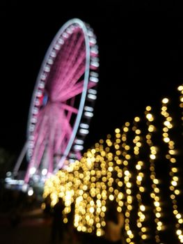 Defocused scene of giant pink flyer ferris wheel at night with yellow light fence