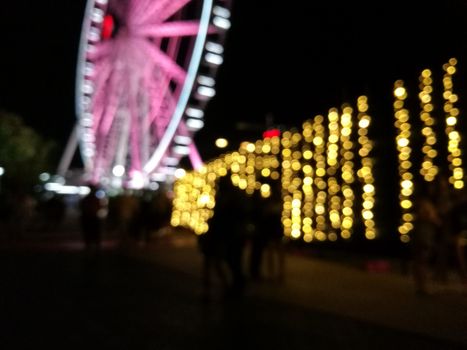 Defocused scene of giant pink flyer ferris wheel at night with yellow light fence