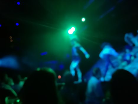 Defocused abstract blurred scene of musical light performance in a concert on stage with crowd