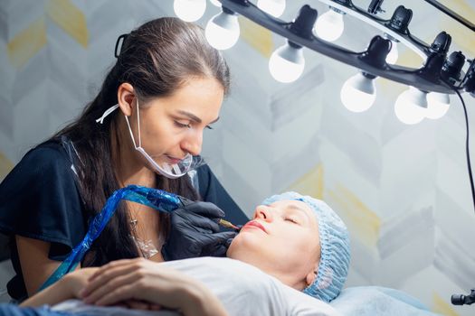 A woman makes permanent lip makeup to another woman in a beauty salon cabinet. Face tattoo. Modern trends in cosmetology