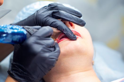 The process of applying permanent makeup on the lips with a tattoo machine close-up. Permanent apparatus needle