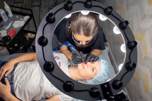 A woman makes permanent lip makeup to another woman in a beauty salon cabinet. Face tattoo. Modern trends in cosmetology