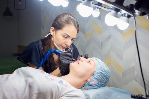 A woman makes permanent lip makeup to another woman in a beauty salon cabinet. Face tattoo. Modern trends in cosmetology