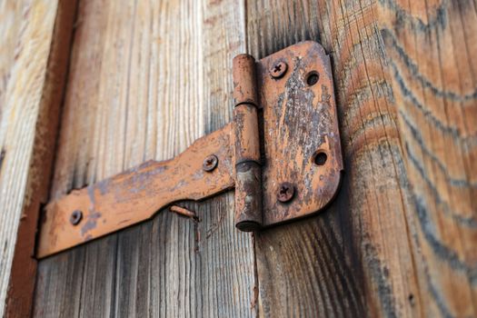 Old and rusty door hinge holding a wooden gate closed