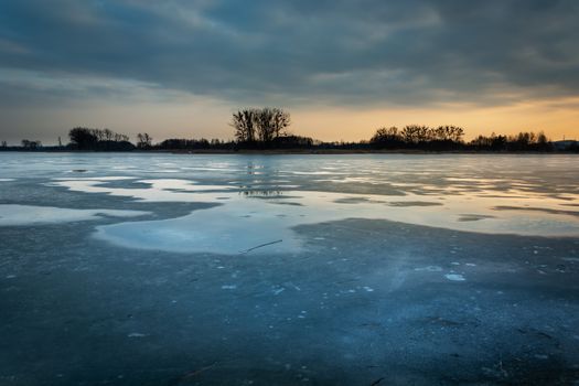 Water puddles on the frozen lake and clouds after sunset, winter evening landscape