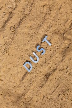 the word dust laid with silver metal letters on dusty road surface - close-up under direct sunlight