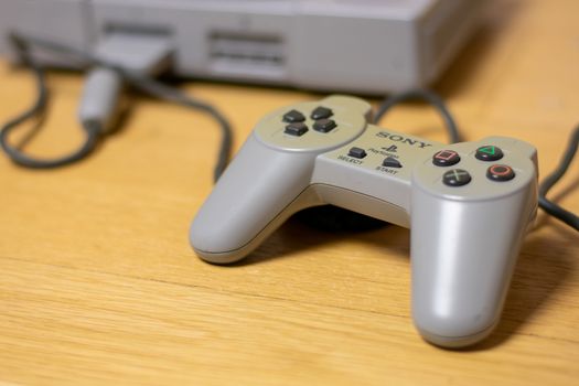 A Controller for the Original Playstation, Plugged Into the Console, on a wood floor.