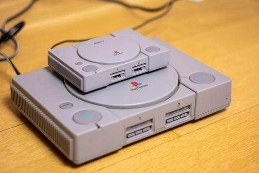 A Playstion Classic On Top of an Original Playstation, a comparison of the two, on a wood floor.