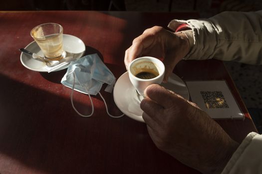 The hands of a man, holds a cup of coffee, while the afternoon light enters through the bar window, Luesia, Aragón, Spain.