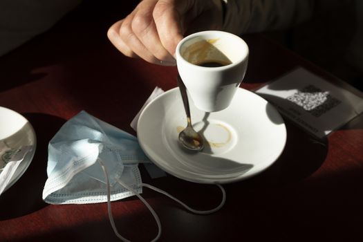 The hand of a man, holds a cup of coffee, while the afternoon light enters through the bar window, Luesia, Aragón, Spain.