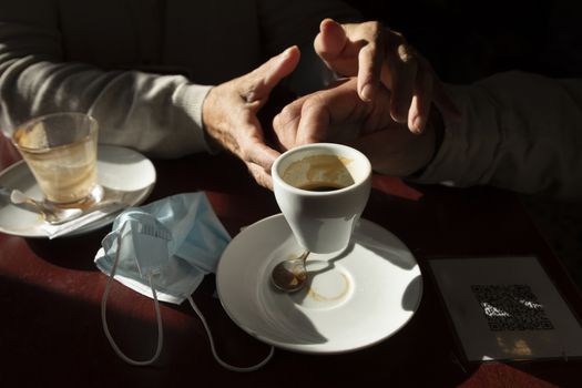 The hand of a man, that holds a cup of coffee, are lovingly picked up by his wife's, while the afternoon light enters through the bar window, Luesia, Aragón, Spain.