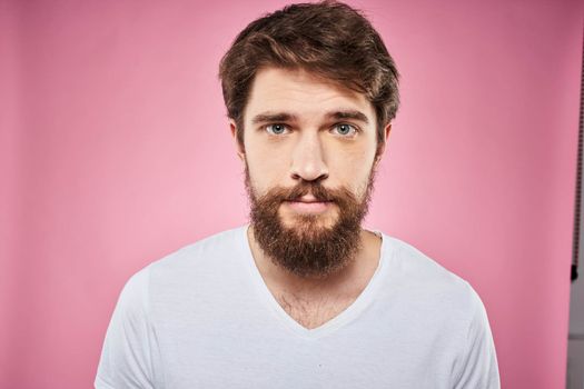 Emotional bearded man in white T-shirt discontent pink background. High quality photo