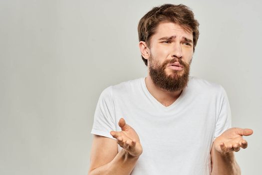 bearded man gesturing with his hands in a white t-shirt aggression light background. High quality photo