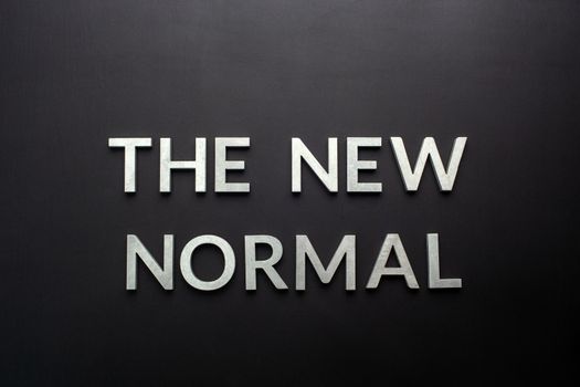 words the new normal laid with silver metal letters on flat black matte surface directly above in flat lay perspective.