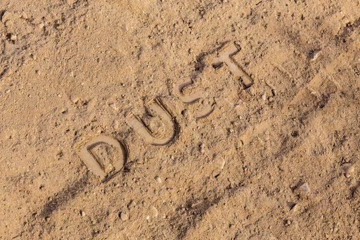 the word dust physically imprinted or embossed on dusty road surface - close-up flat lay perspective under direct sunlight