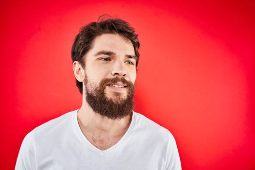 A man in a white T-shirt with a beard gestures with his hands emotions red background. High quality photo