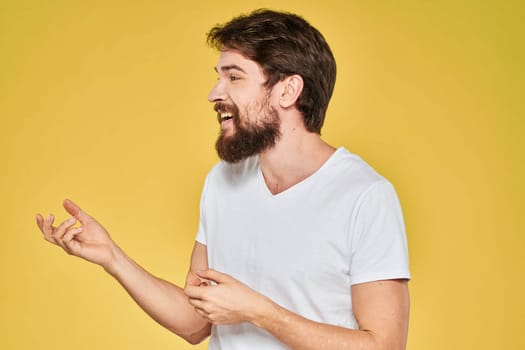 Bearded man white t-shirt emotions gestures with hands fun yellow background. High quality photo