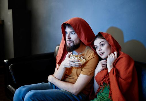 a man and a woman with a red plaid on their heads are sitting on the sofa in front of the TV indoors. High quality photo