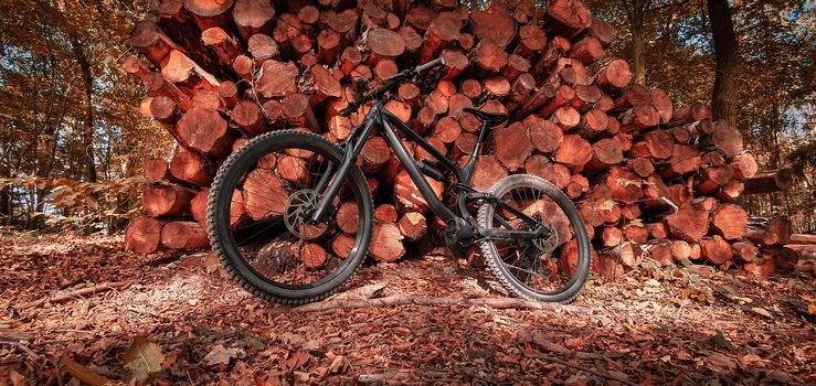 Full suspension mountain bike leaned on a stacked pile of timber logs in a beautiful autumn forest trail. Mountain biking concept. Freedom and recreation concept.