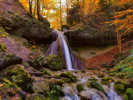 Waterfall in autumn with orange and yellow colors. Running clear, cold water in a forrest during autumn.