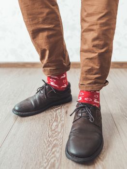 Young man pulls up leg of his chinos trousers to show bright red socks with reindeers on them. Scandinavian pattern. Winter holiday spirit. Casual outfit for New Year and Christmas celebration.