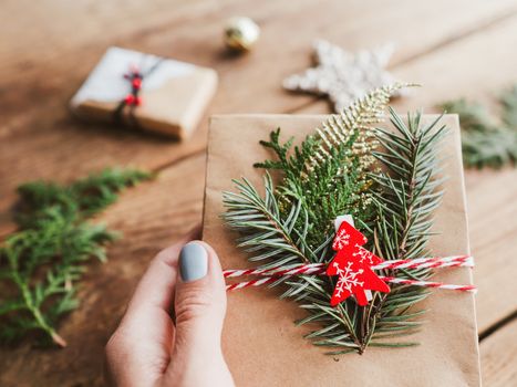 Christmas DIY presents wrapped in craft paper with fir tree twigs. Red decorations in shape of Christmas tree, stars. New Year gifts on wooden background. Winter holiday spirit.