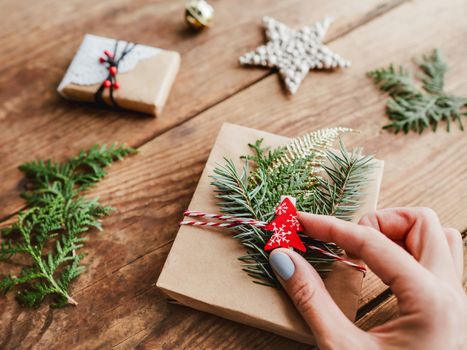 Christmas DIY presents wrapped in craft paper with fir tree twigs. Red decorations in shape of Christmas tree, stars. New Year gifts on wooden background. Winter holiday spirit.