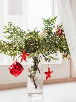 Vase with decorated thuja branches stands on window sill. Sustainable alternative for Christmas tree. Caring for nature. Refusal to cut down spruce forests. New Year celebration.