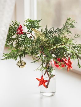Vase with decorated thuja branches stands on window sill. Sustainable alternative for Christmas tree. Caring for nature. Refusal to cut down spruce forests. New Year celebration.