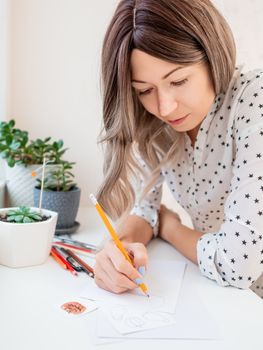 Woman draws ghosts and pumpkins. Handmade decorations for Halloween. DIY stickers on for flower pots. Socially-Distanced Halloween at home.