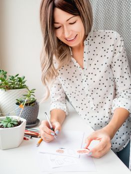 Woman decorates flower pots with handmade Halloween stickers. Hand drawn ghosts, flags and pumpkins in flower pot with succulent plant.