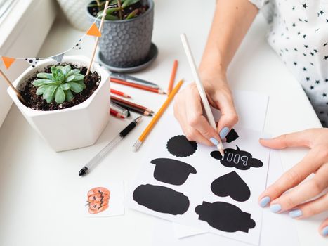 Woman writes Boo! on decorative black stickers for flower pots. Handmade decorations for Halloween.