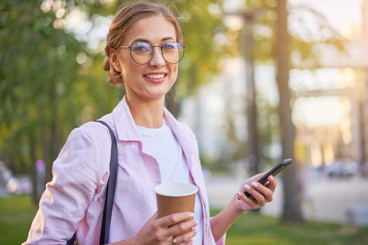 Businesswoman standing summer park Business person using smartphone Outdoors Successful european caucasian woman freelancer or teacher walking outside backpack dressed jeans white shirt pink jacket