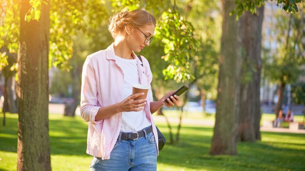 Businesswoman standing summer park Business person using smartphone Outdoors Successful european caucasian woman freelancer or teacher walking outside backpack dressed jeans white shirt pink jacket