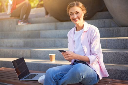 Businesswoman sitting stairs summer park using laptop and smartphone Business persone working remote. Outdoor. Successful Young european caucasian woman freelancer meeting online