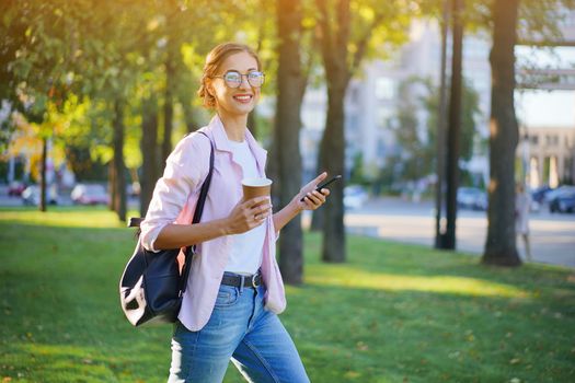 Businesswoman standing summer park Business person using smartphone Outdoors Successful european caucasian woman freelancer or teacher walking outside backpack dressed jeans white shirt pink jacket