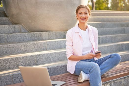 Businesswoman sitting stairs summer park using laptop and smartphone Business persone working remote. Outdoor. Successful Young european caucasian woman freelancer meeting online