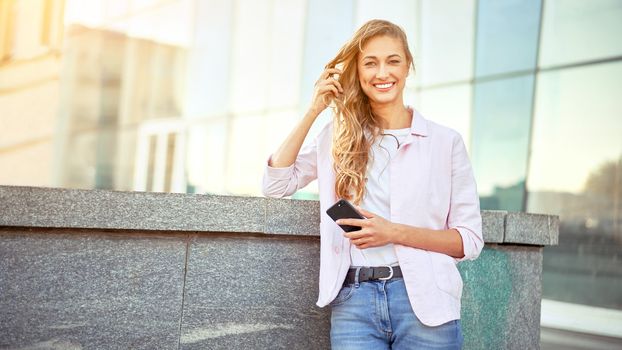 Businesswoman standing summer day near corporate building using smartphone teeth smiling Business person Outdoors Successful european caucasian woman freelancer dressed white shirt pink jacket