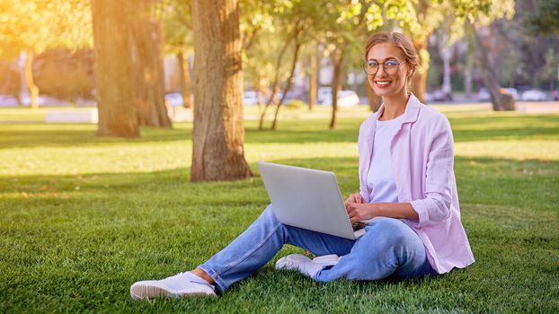 Businesswoman sitting grass summer park using laptop Business person working remote. Outdoor Successful european caucasian woman freelancer make video call teacher study work online lessons