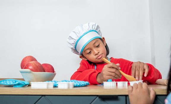 Cute girl in chef uniform and simulated cooking toys in the kitchen counter.