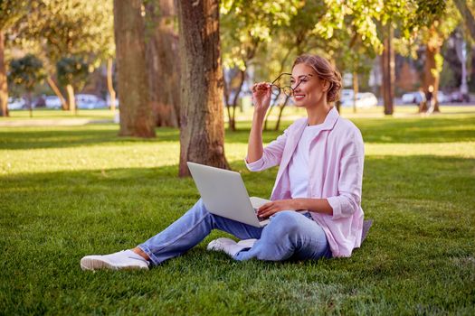 Businesswoman sitting grass summer park using laptop Business person working remote. Outdoor Successful european caucasian woman freelancer make video call teacher study work online lessons