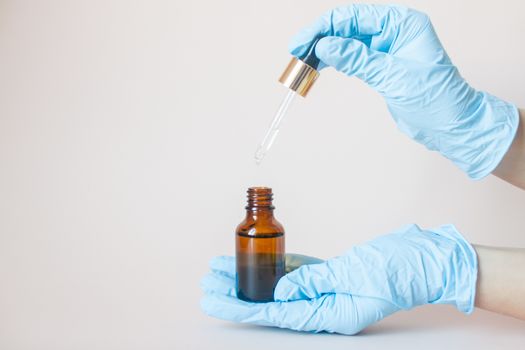 Bottles with serum for the face in his hands in protective medical rubber gloves on a light background. Beauty industry.